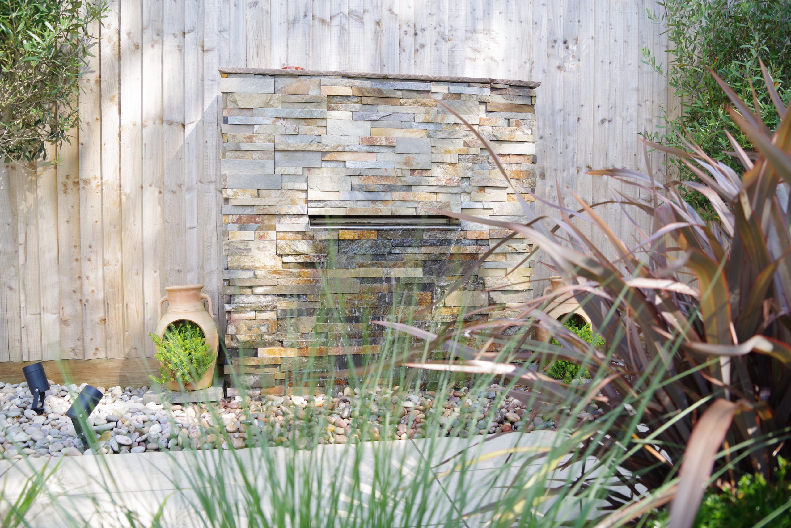 A waterfall feature with split face tile cladding, surounded by terracotta pots.